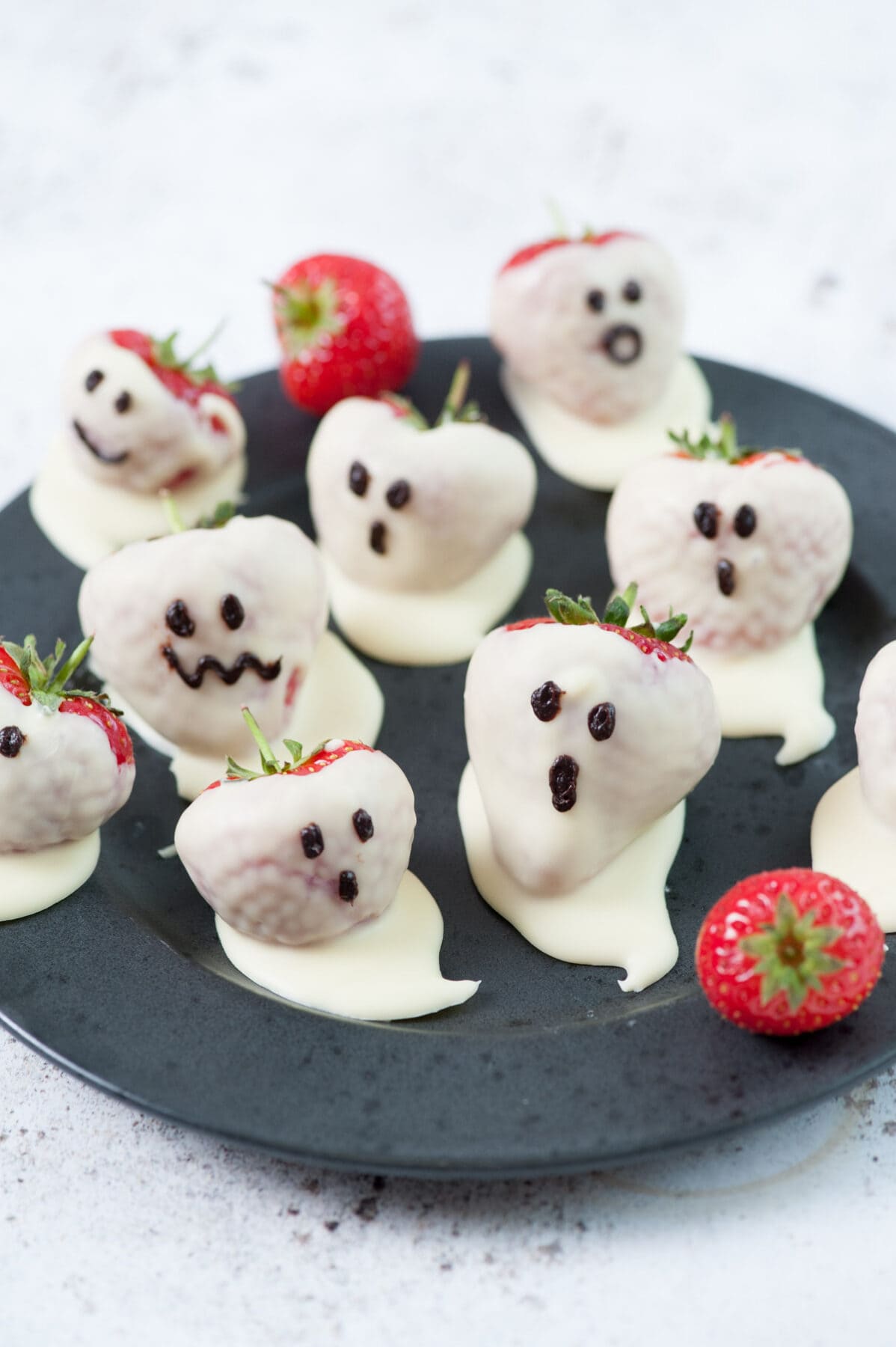 White chocolate covered strawberries (Strawberry ghosts) on a black plate.