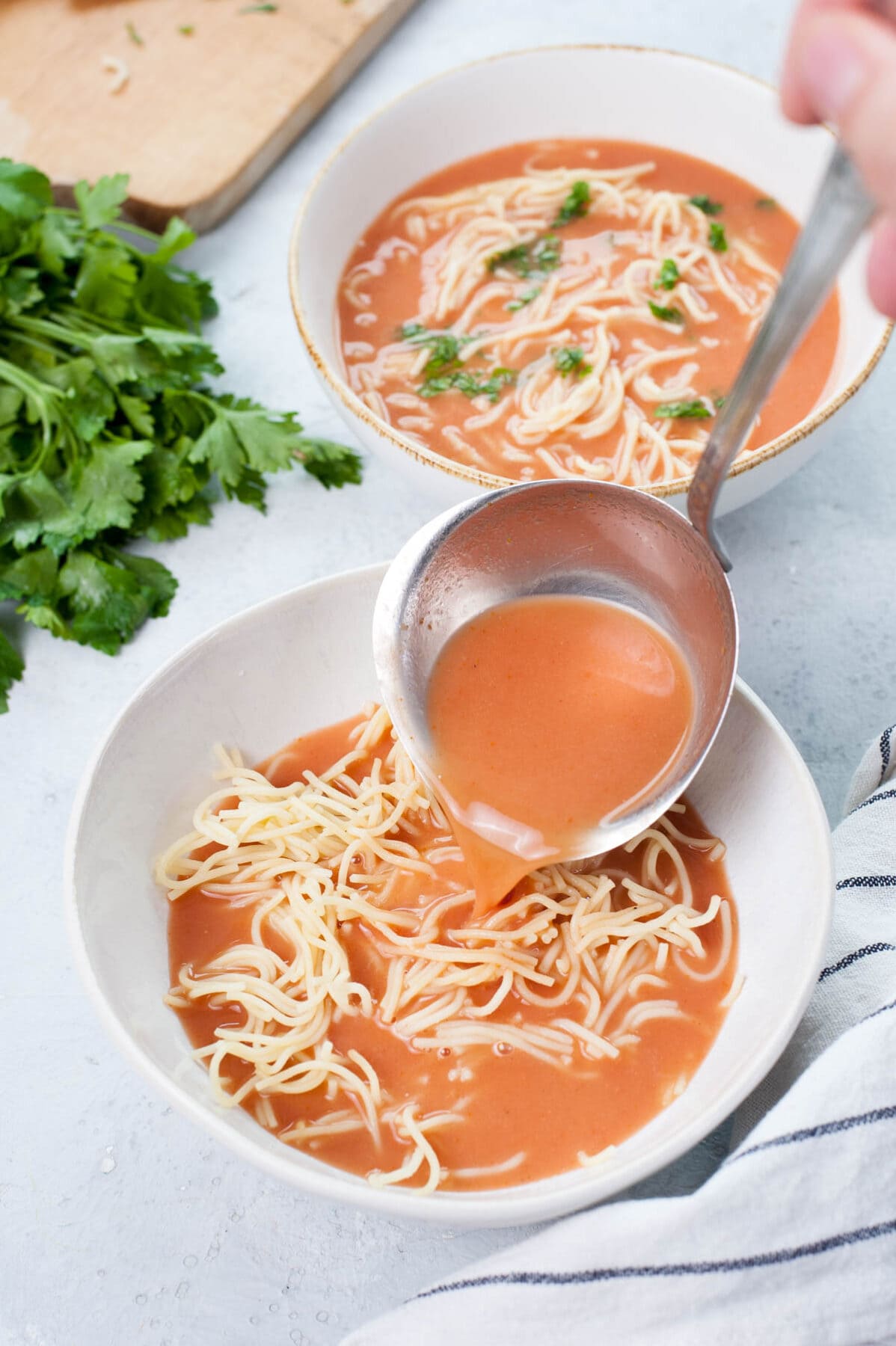 Tomato soup is being poured into a plate with cooked noodles.