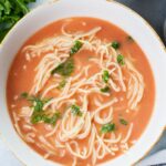 Polish tomato soup served with noodles and chopped parsley in a white bowl.