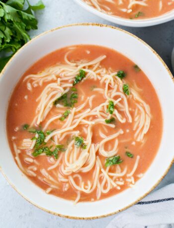 Polish tomato soup served with noodles and chopped parsley in a white bowl.