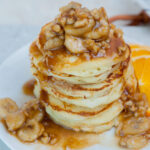 A stack of bananas foster pancakes on a white plate.