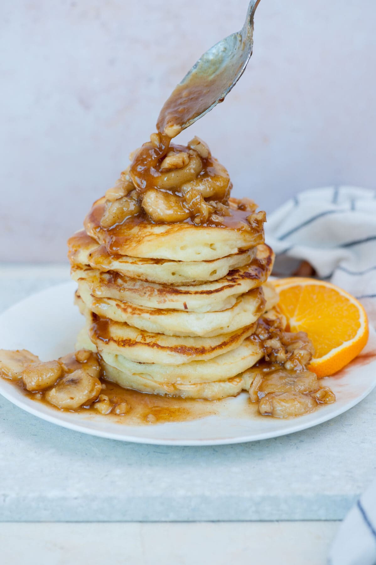 Bananas foster topping is being spooned over a stack of pancakes.