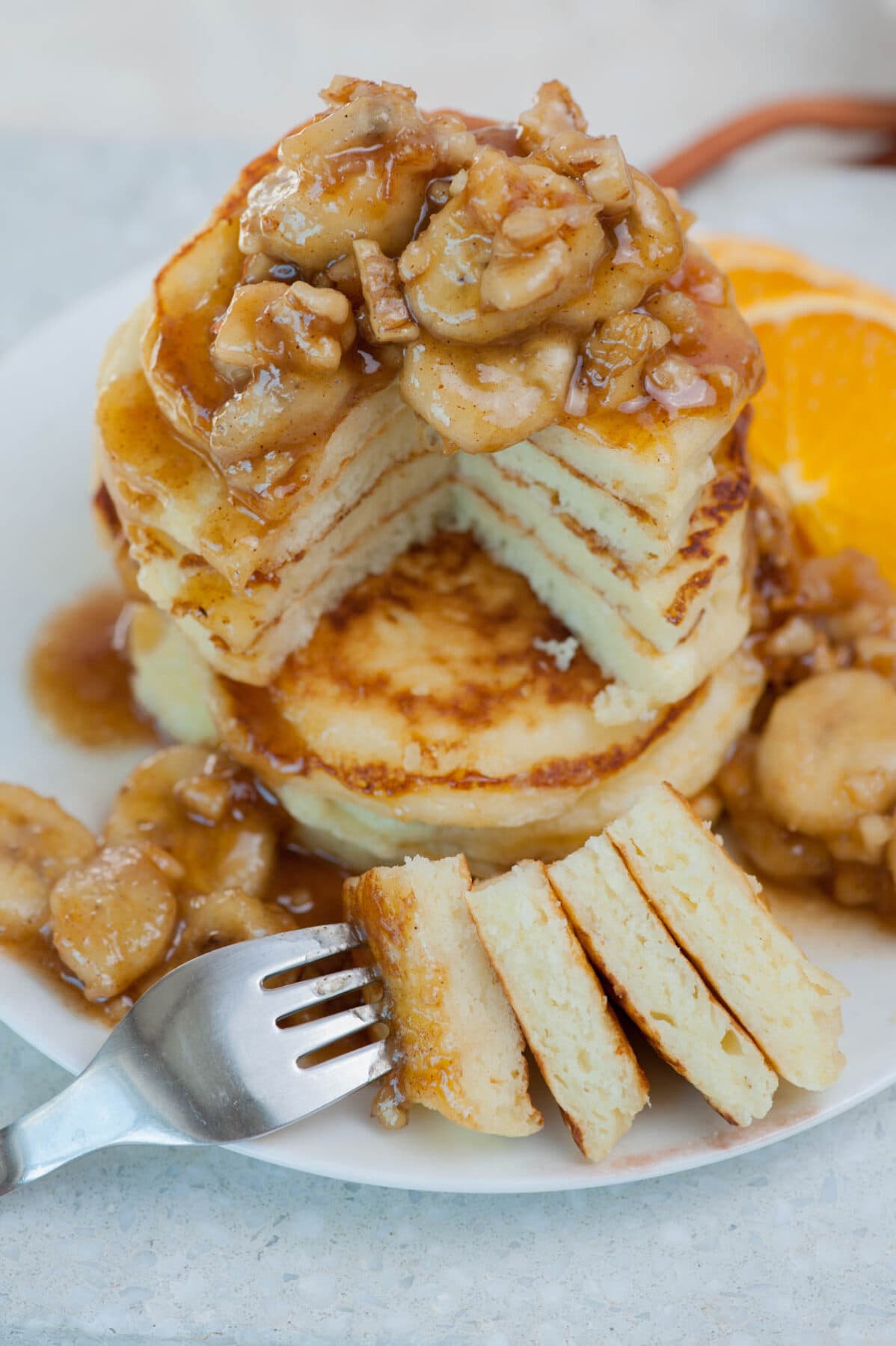 A stack of banana foster pancakes with a part cut of and stuck on a fork.