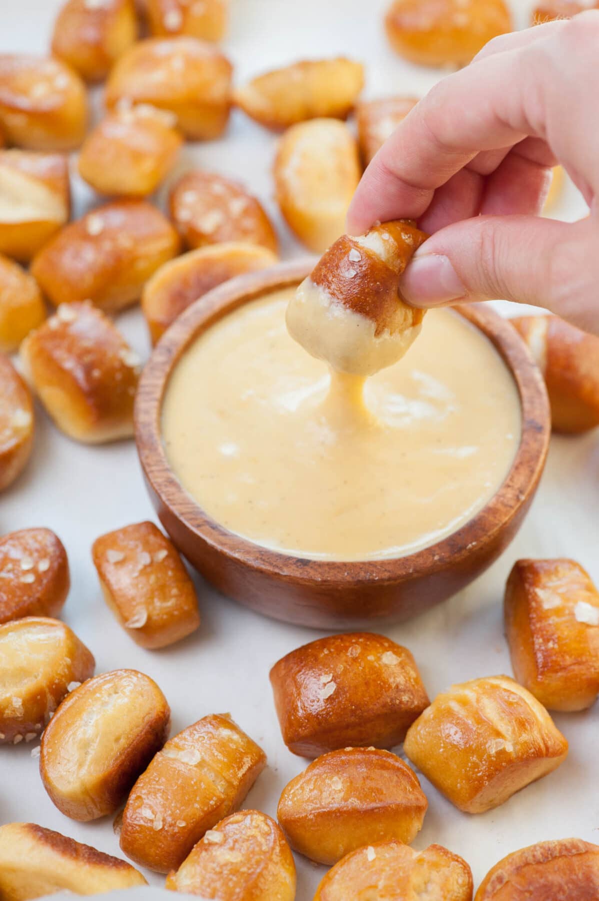 Soft pretzel bites are being dipped in beer cheese dip in a brown bowl.