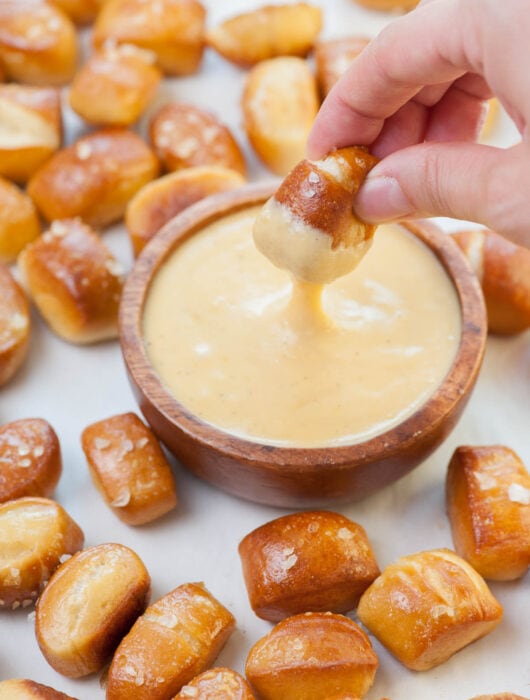 Beer cheese dip in a brown bowl surrounded with soft pretzel bites.