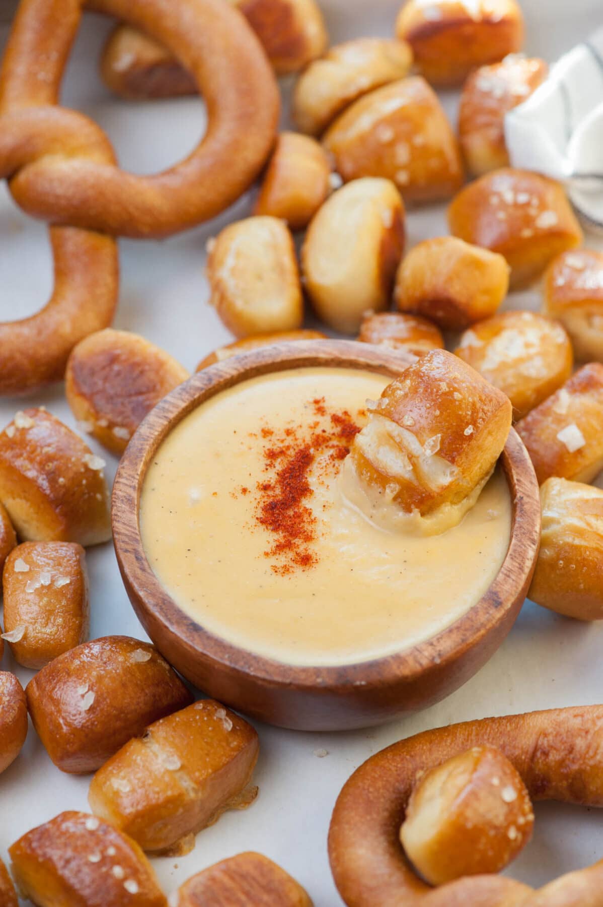 A brown bowl with beer cheese dip surrounded by soft pretzel bites. One pretzel bite in a bowl with the sauce.