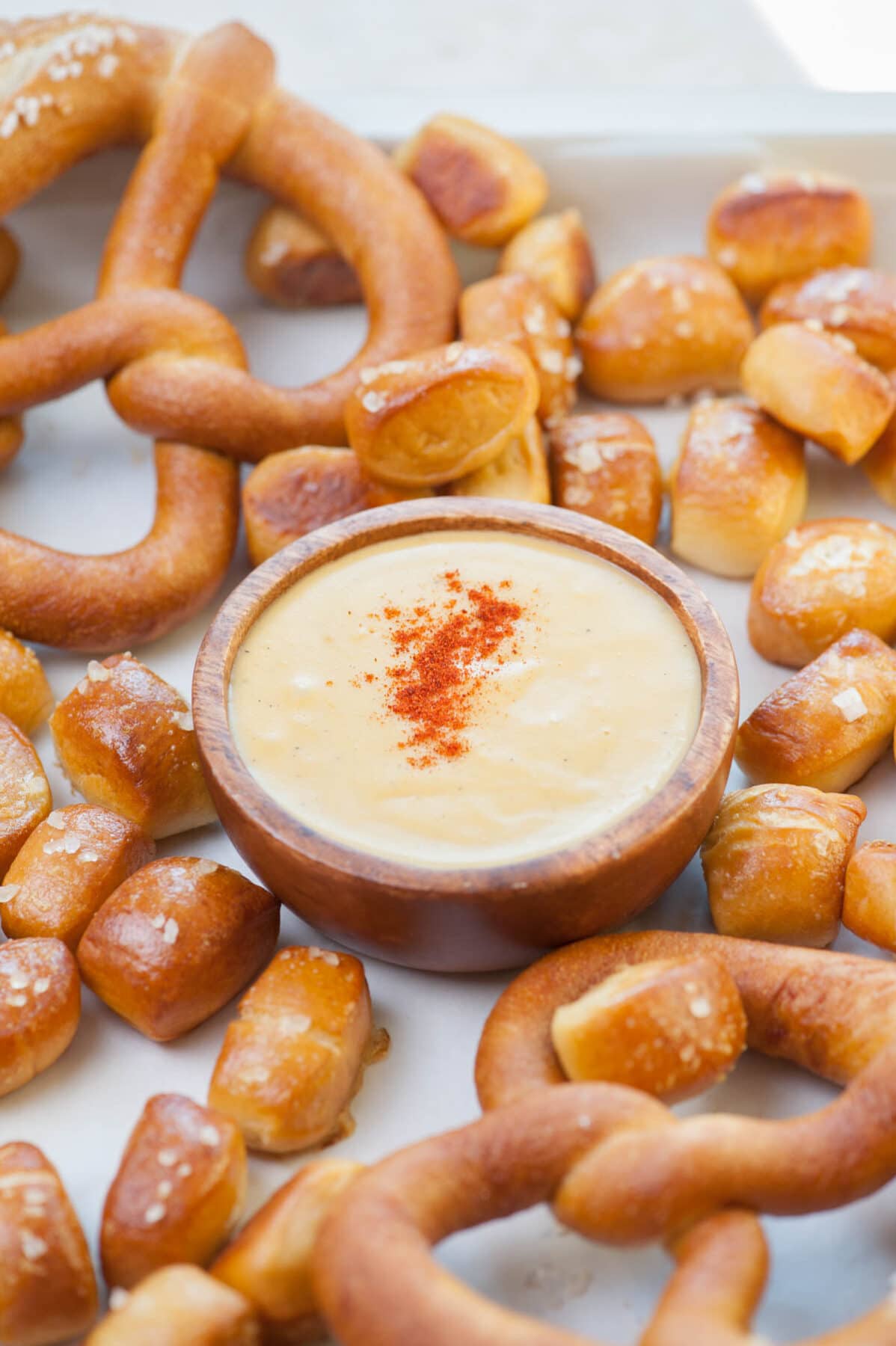 A brown bowl with beer cheese dip surrounded by soft pretzel bites.