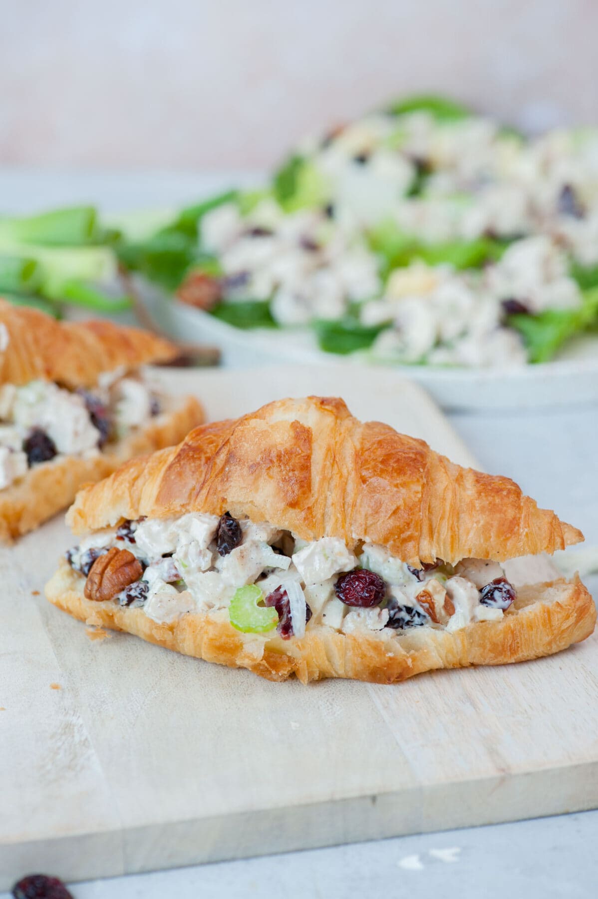 Croissant sandwich with cranberry chicken salad on a beige wooden board.
