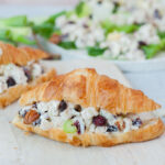 Cranberry chicken salad croissant sandwich on a white cutting board.