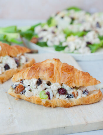 Cranberry chicken salad croissant sandwich on a white cutting board.