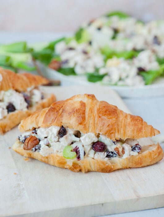 Cranberry chicken salad croissant sandwich on a white cutting board.