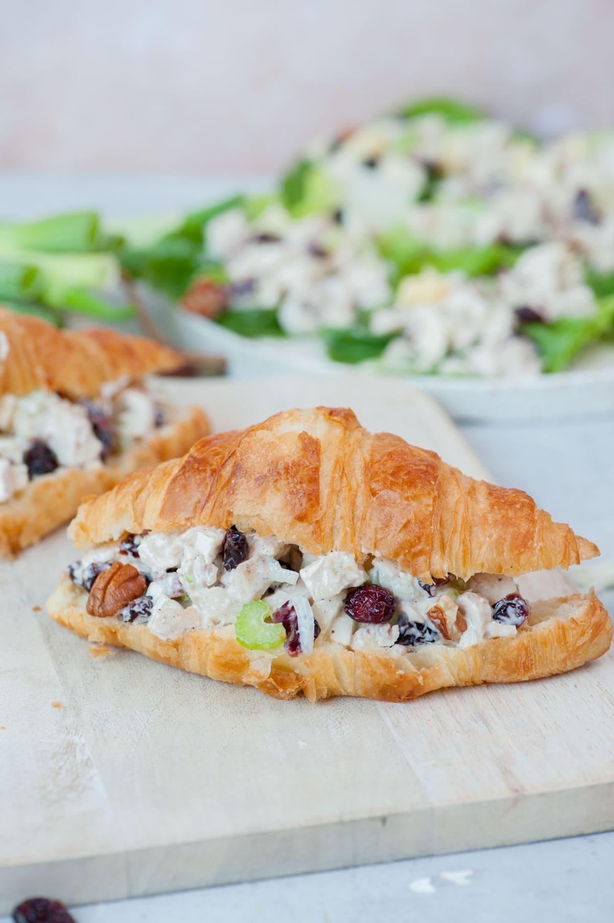 Cranberry chicken salad croissant sandwich on a white cutting board.