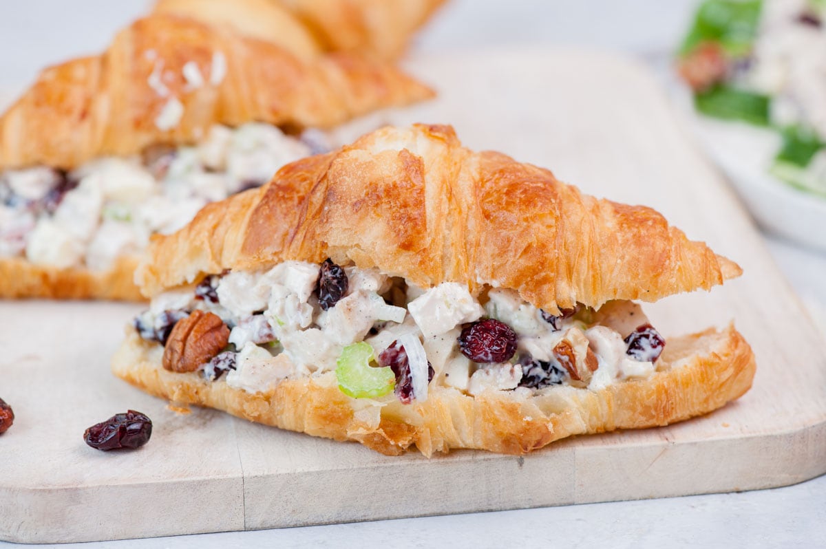 Croissant sandwich with cranberry chicken salad on a beige wooden board.