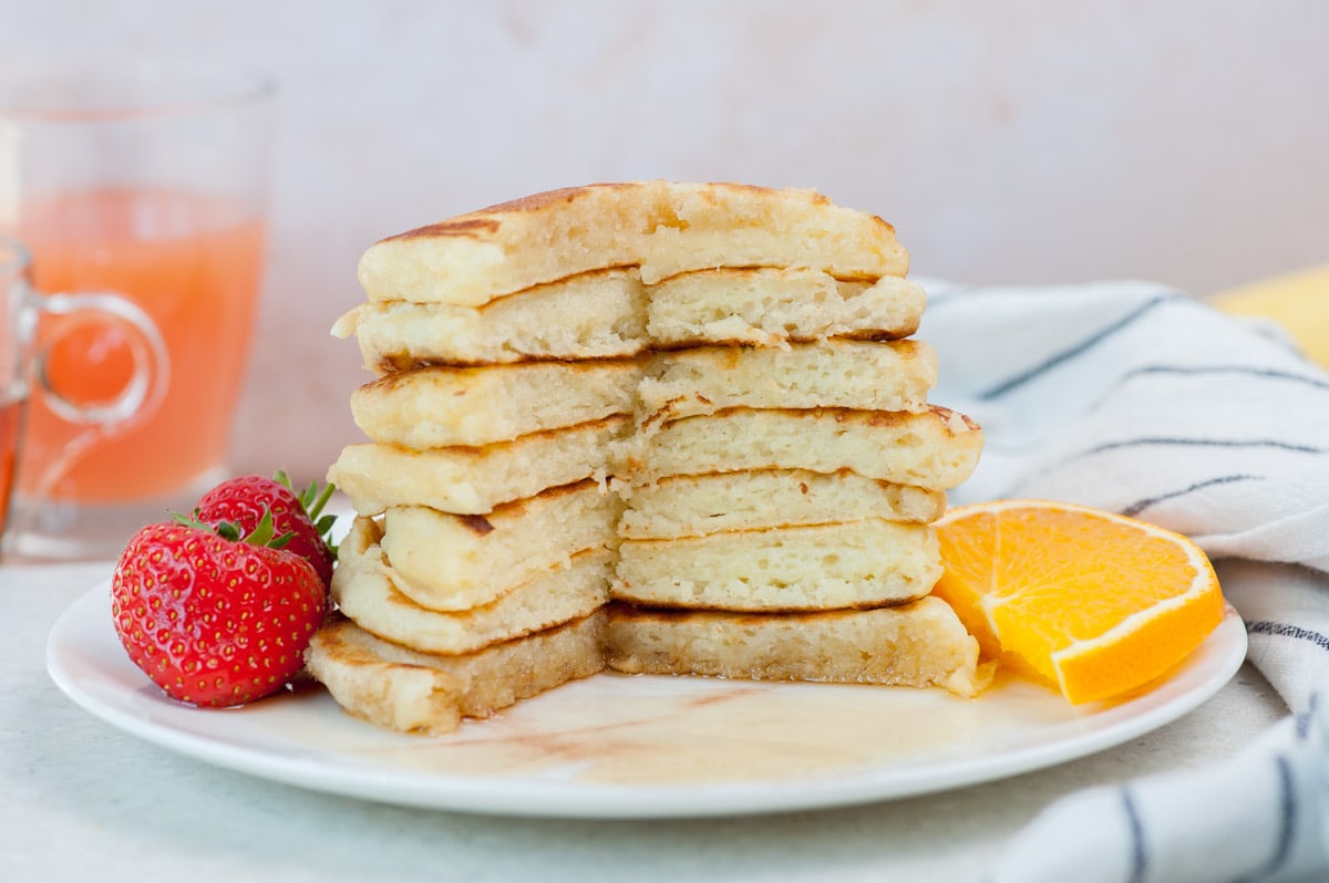 A stack of buttermilk pancakes on a white plate with fresh fruit.