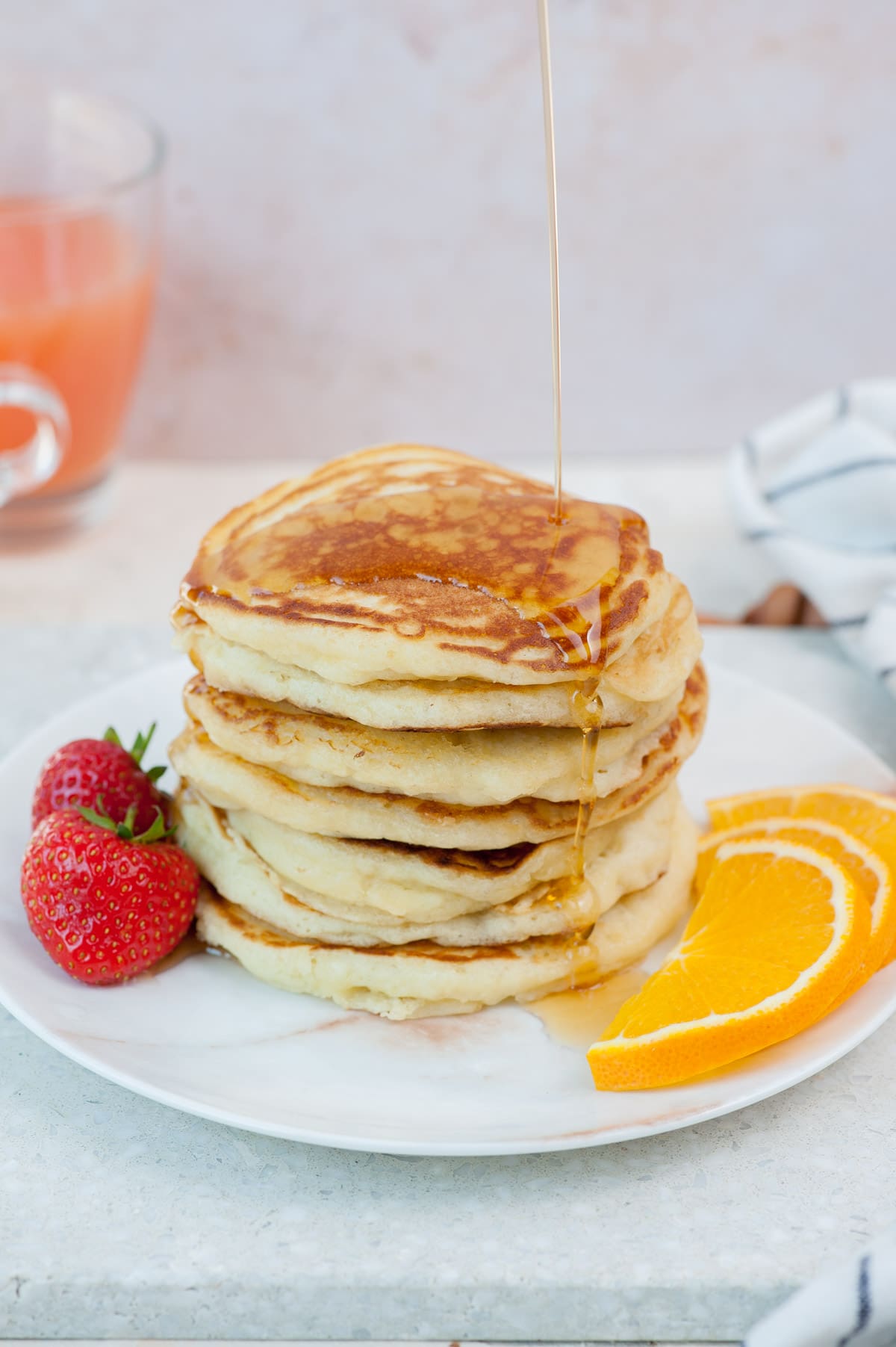 A stack of buttermilk pancakes is being poured with maple syrup.