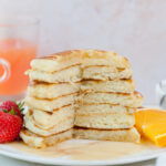 A stack of buttermilk pancakes with a part missing on a white plate.