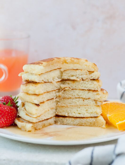 A stack of buttermilk pancakes with a part missing on a white plate.