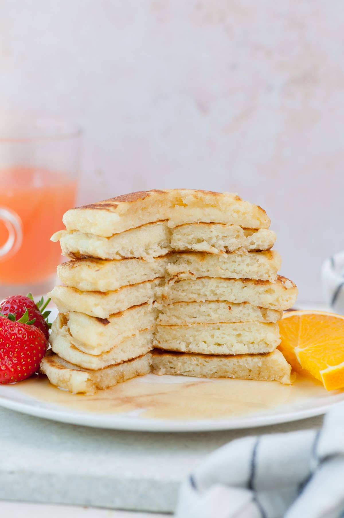 A stack of buttermilk pancakes on a white plate with fresh fruit.