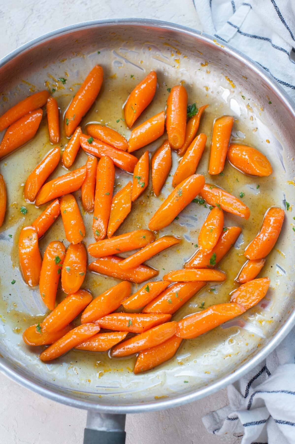 Honey glazed carrots in a frying pan sprinkled with parsley.