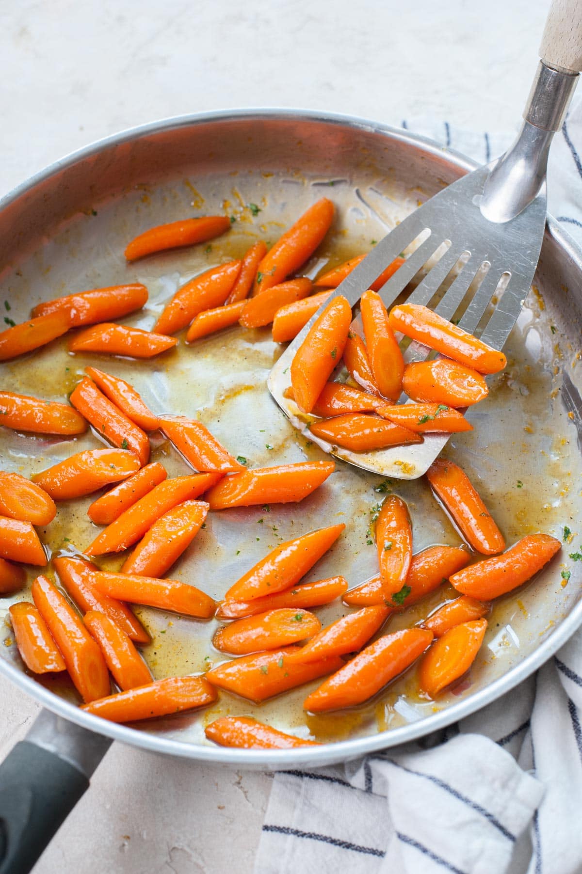 Honey glazed carrots are being scooped with a spatula from a frying pan.