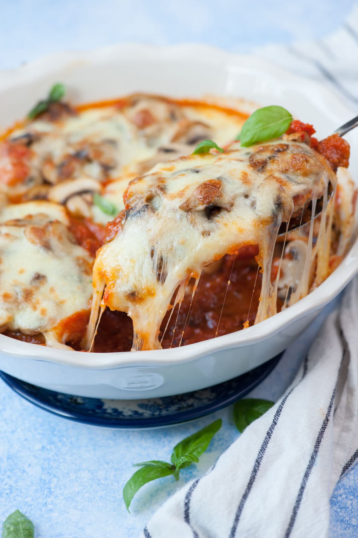 Mozzarella chicken on a spatula is being taken out of a baking dish.