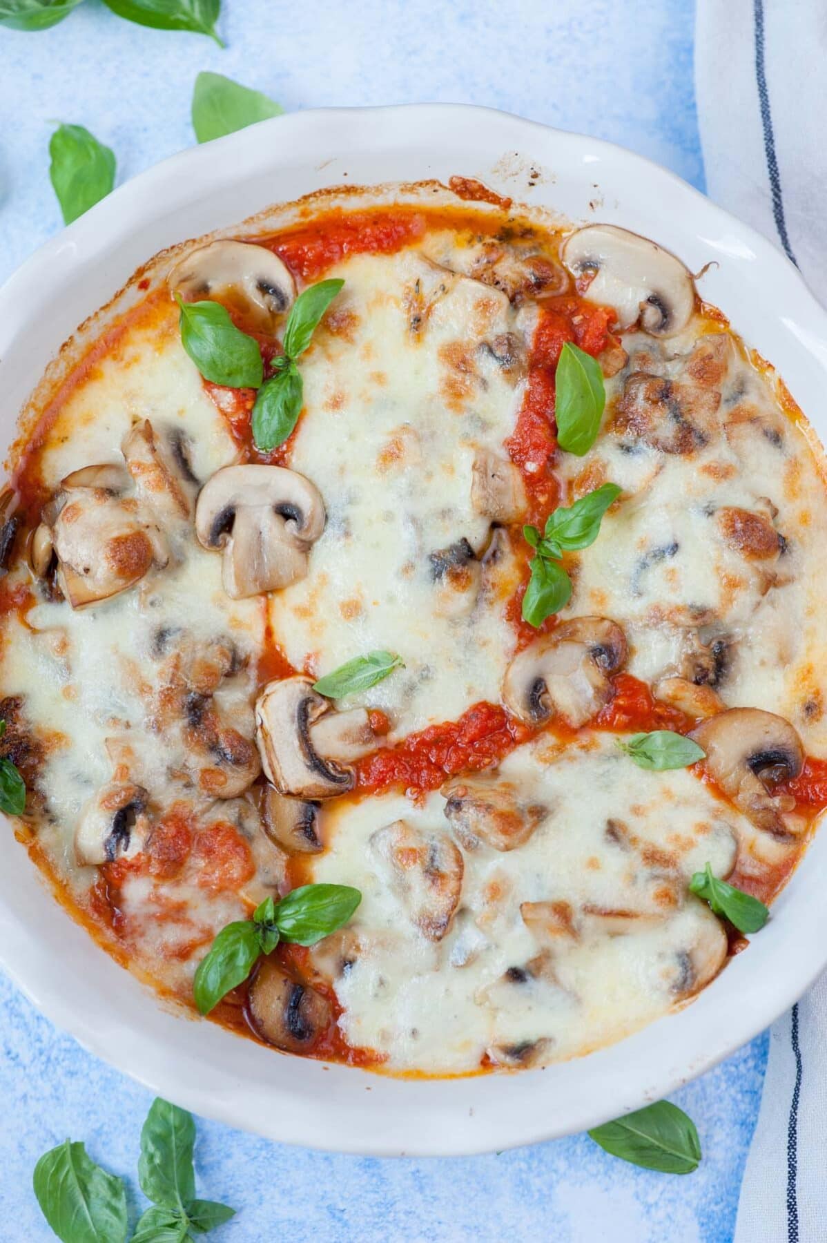 Mozzarella chicken with mushrooms in a white baking dish topped with fresh basil leaves.