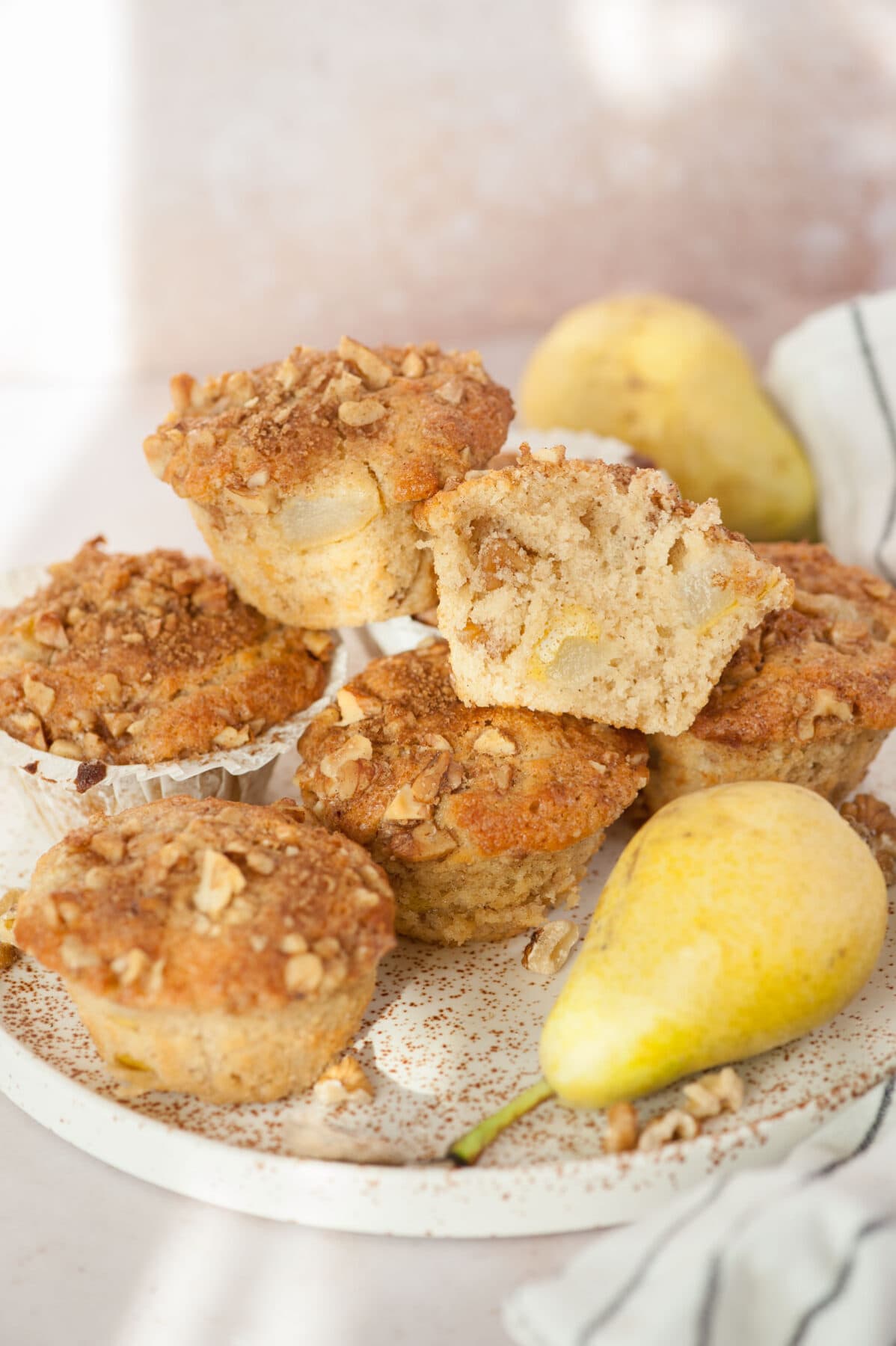 Pear muffins, pears, and walnuts on a white plate. One muffin cut in half.