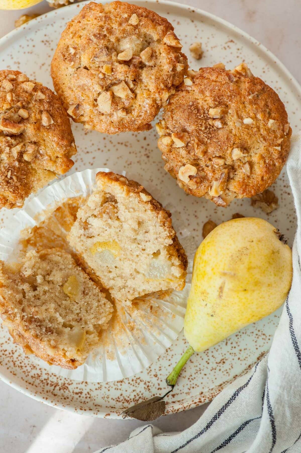 Pear muffins, walnuts, and pears on a white plate. One muffin cut in half. View from above.