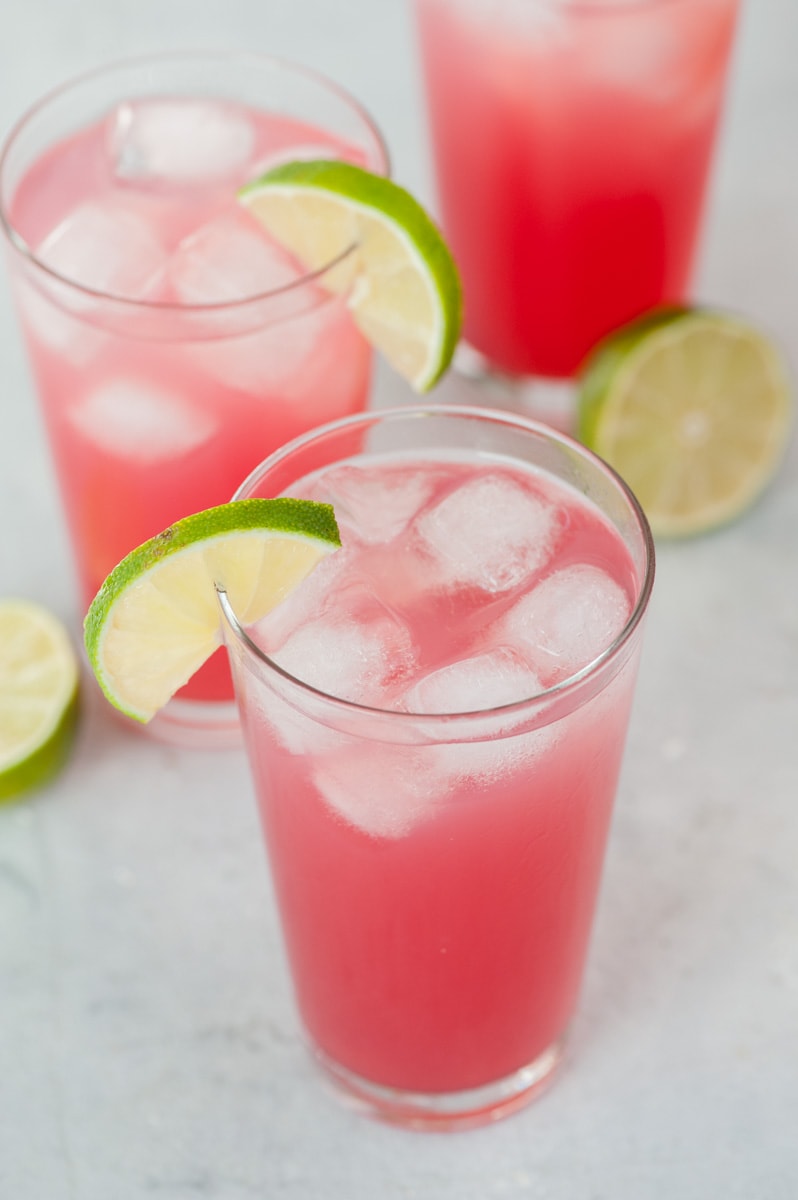 3 glasses with sea breeze cocktail garnished with lime slices.