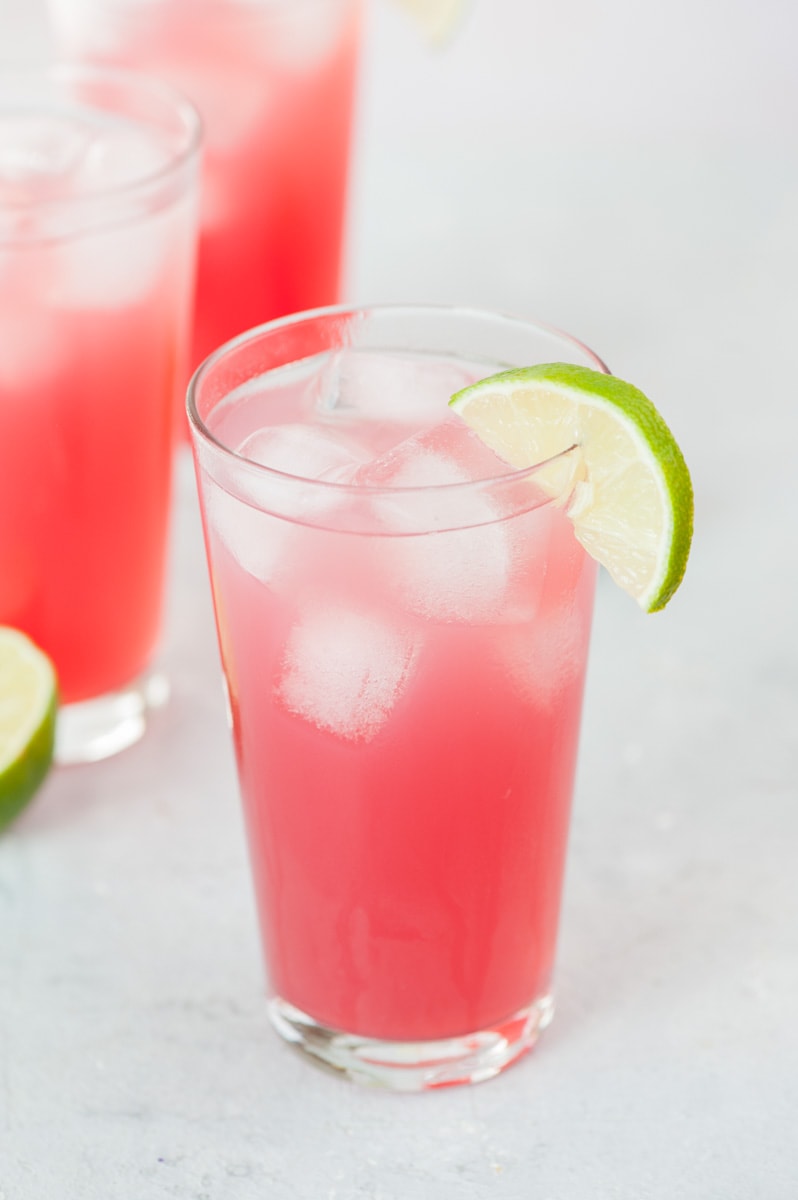 A tall glass with sea breeze cocktail garnished with lime slice.