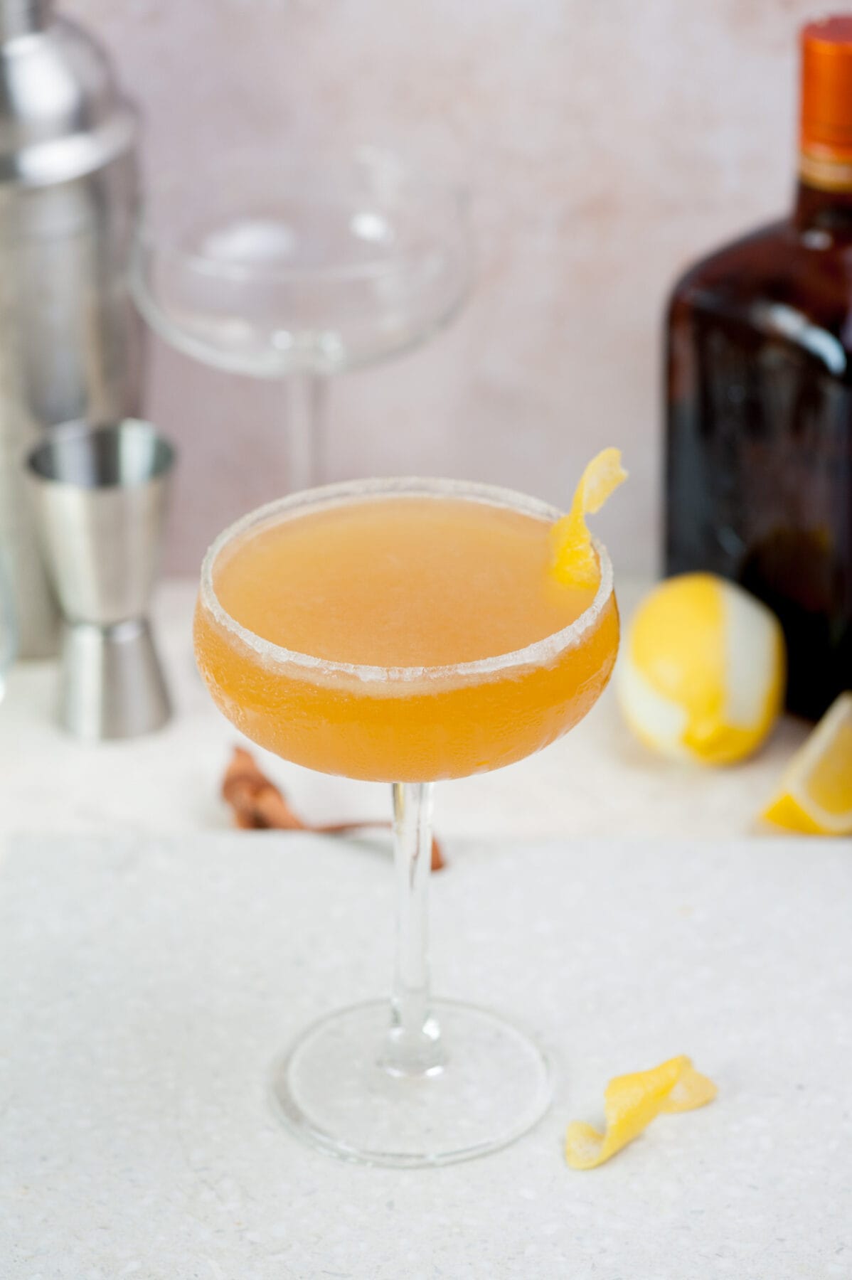 A coupe glass with sidecar cocktail on a grey stone board. A shaker and liqueur bottle in the background.