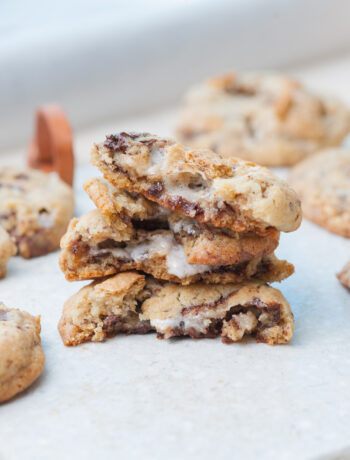 Stacked s'mores cookies torn in half on a light grey background.