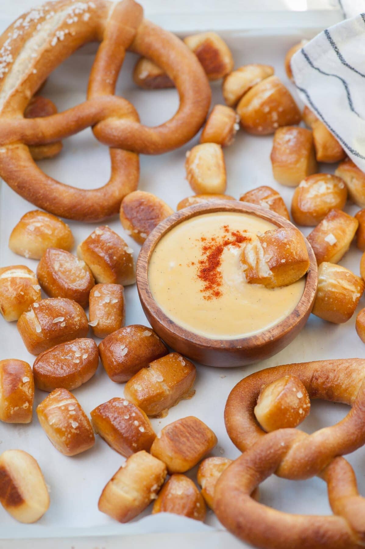 Pretzel bites, large pretzels, cheese sauce on a tray lined with parchment paper.