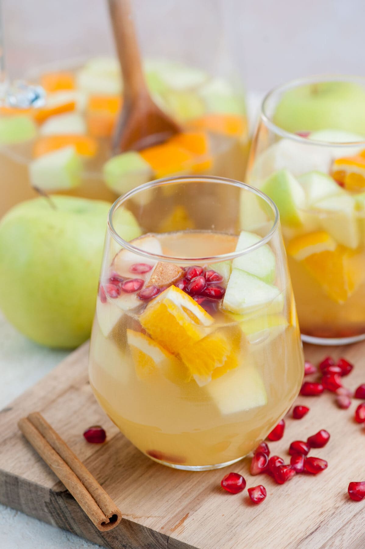 A glass with apple cider sangria and fruit. A pitcher in the background.