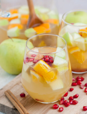 Two glasses with apple cider sangria on a wooden board.