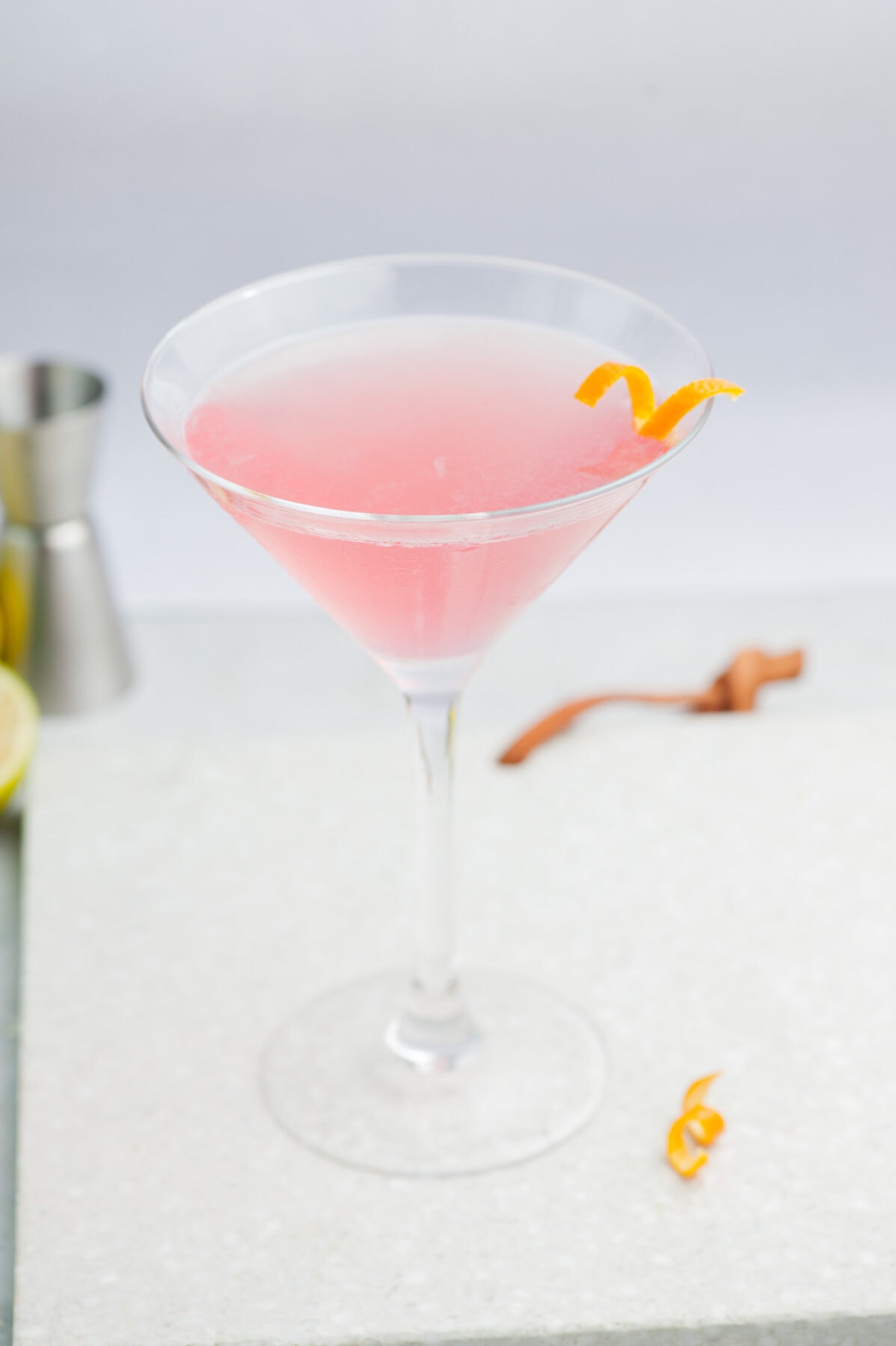 Cosmopolitan cocktail in a martini glass on a grey background, garnished with an orange twist.