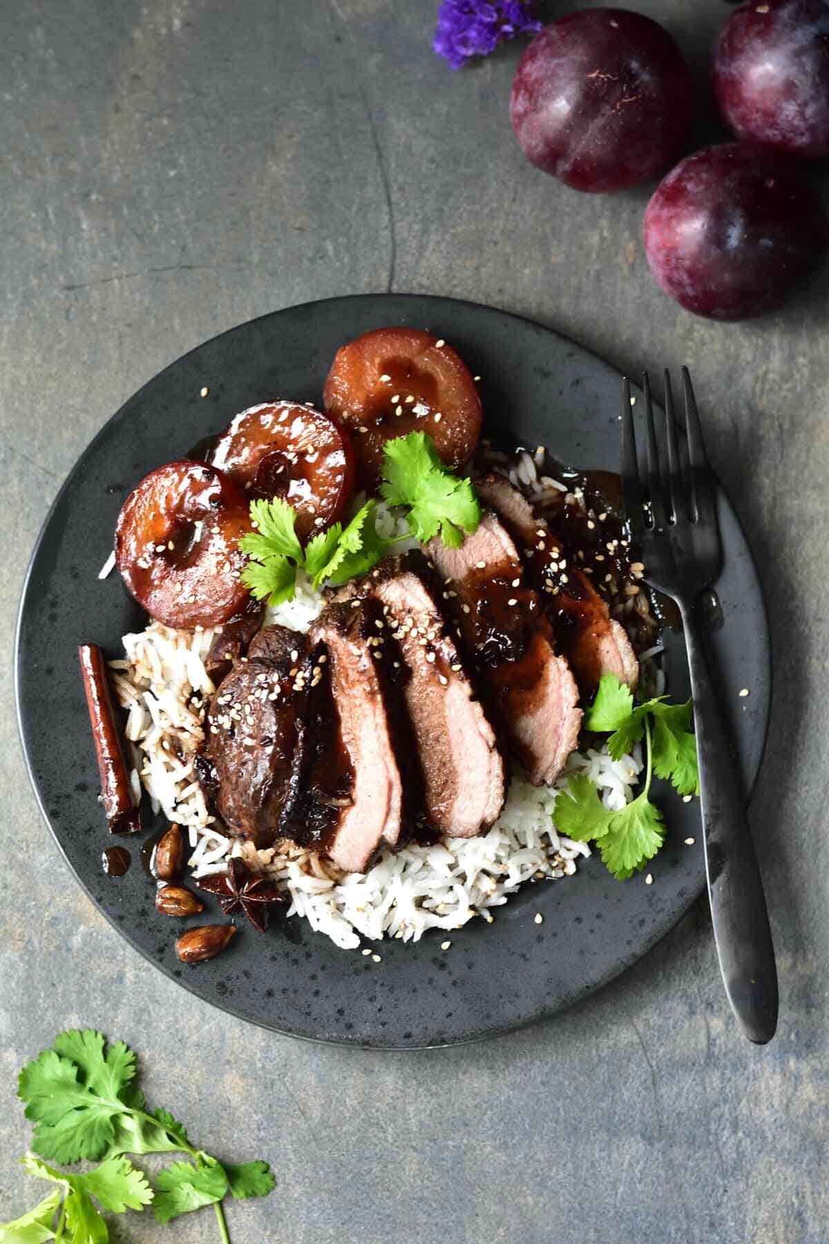 Duck breast with plum sauce and rice on a black plate.