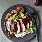 Duck breast with plum sauce on a black plate.