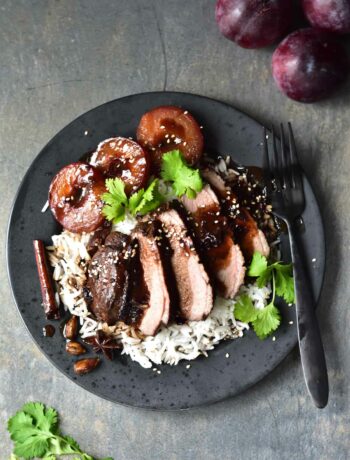 Duck breast with plum sauce on a black plate.