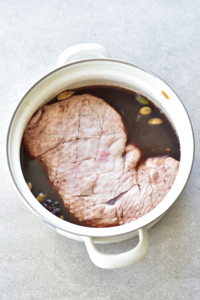 Duck breast in the plum marinade in a white pot.