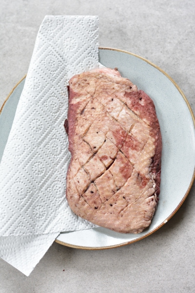 Marinated duck breast on a blue plate with paper towels on the side.