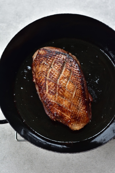 Duck breast is being pan-fried in a black pan.