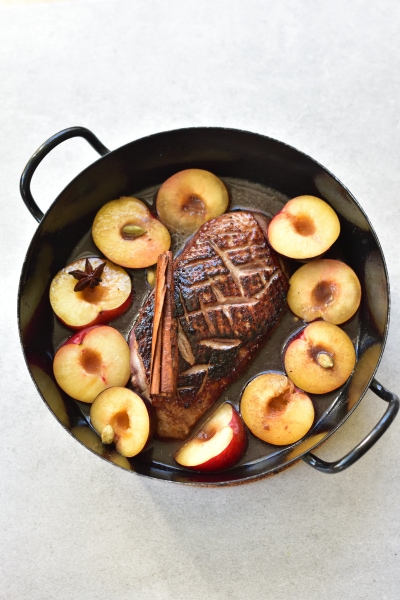 Duck breast with plums and plum sauce in a black pan.