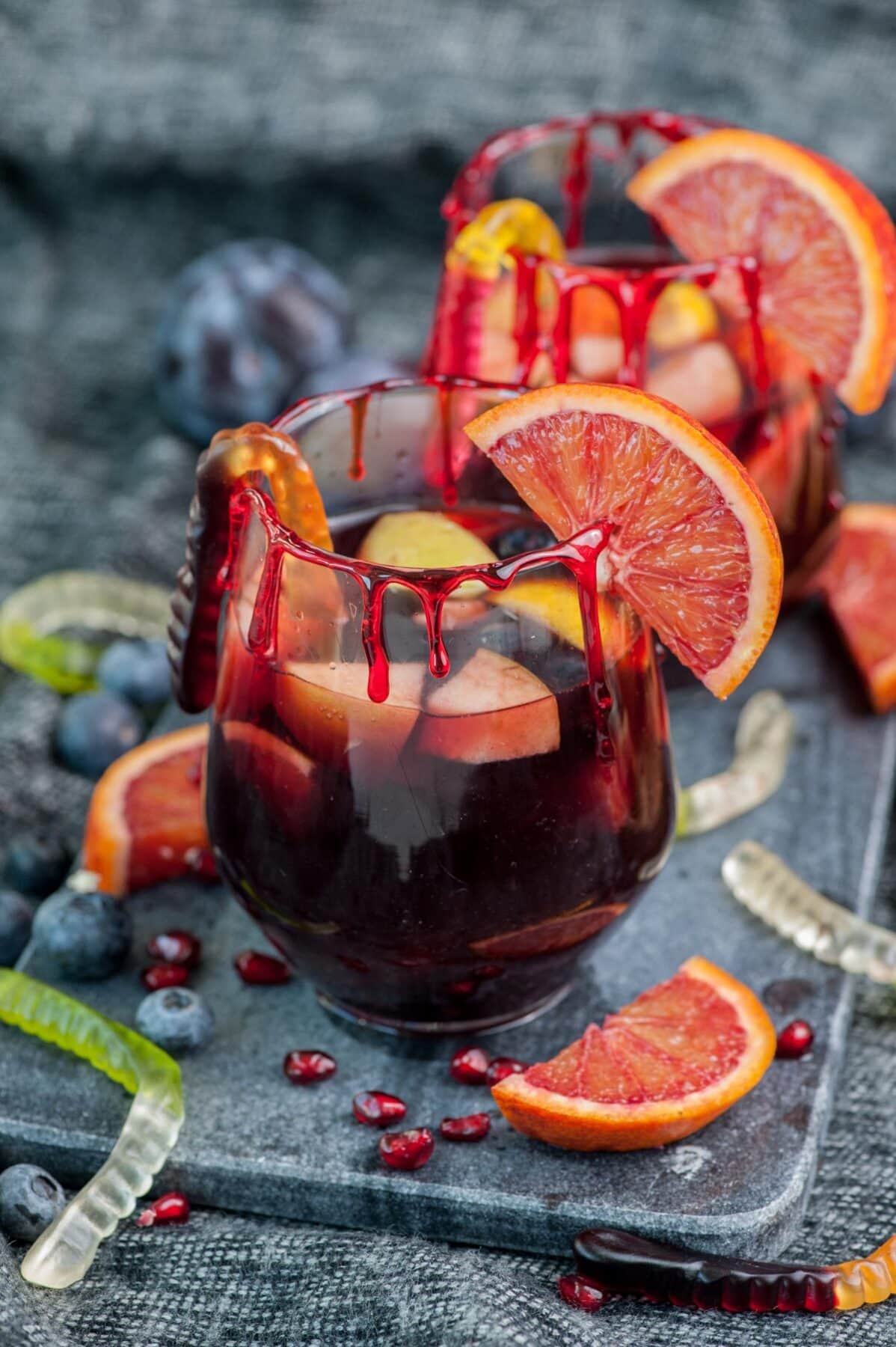 Two glasses with sangria garnished with blood orange slices and fake blood drips.