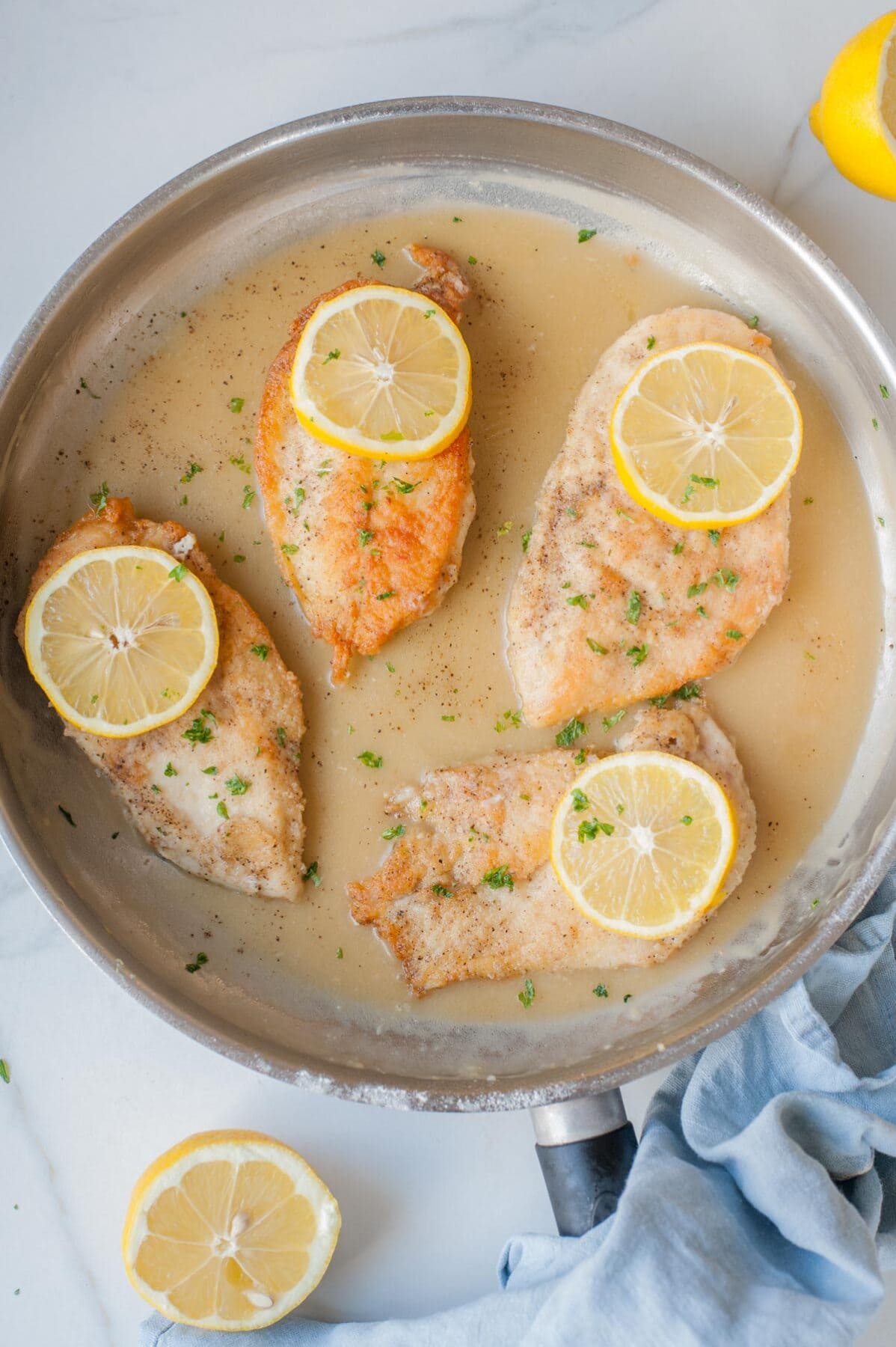 Pan-fried chicken fillets with lemon butter sauce topped with lemon slices in a frying pan.