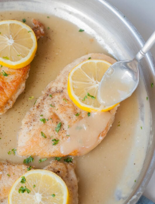 Pan-fried chicken fillet in a frying pan is being poured with lemon butter sauce.