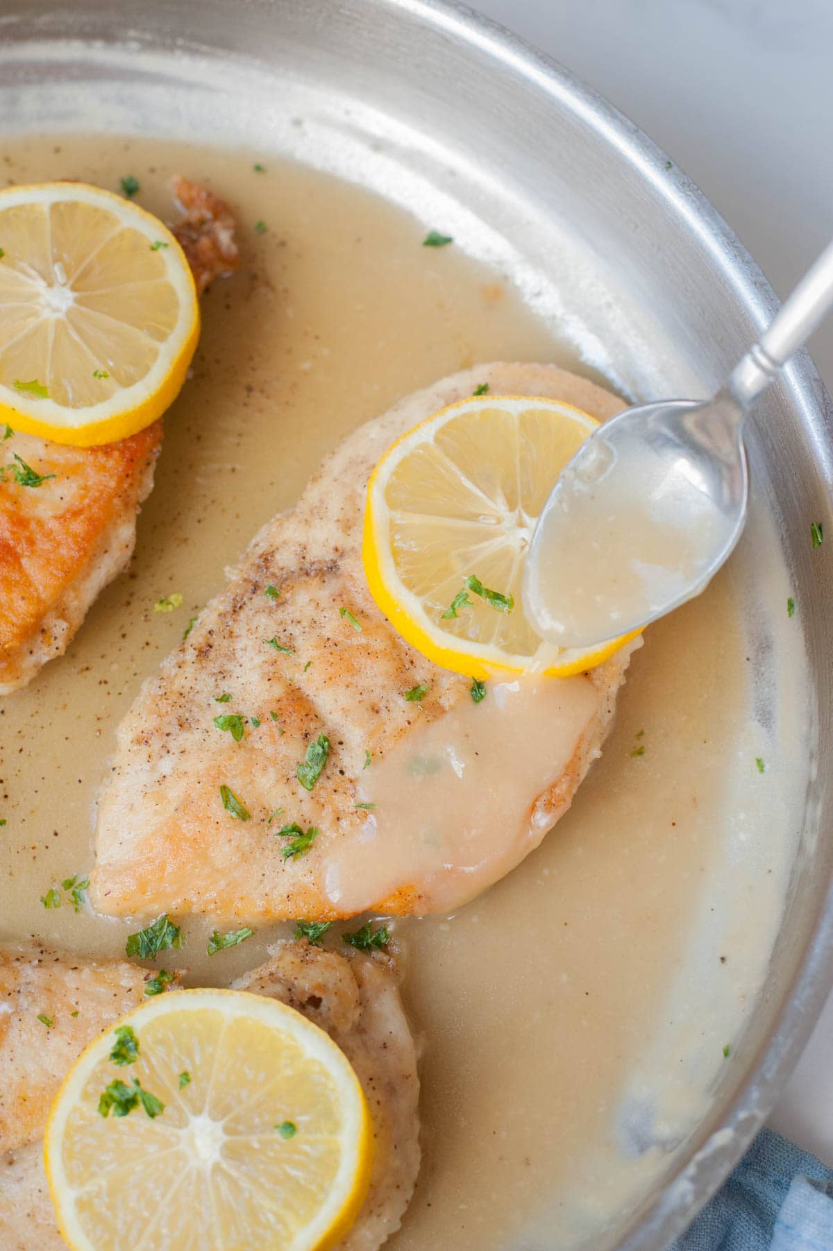Chicken fillet is being poured with lemon butter sauce in a frying pan.