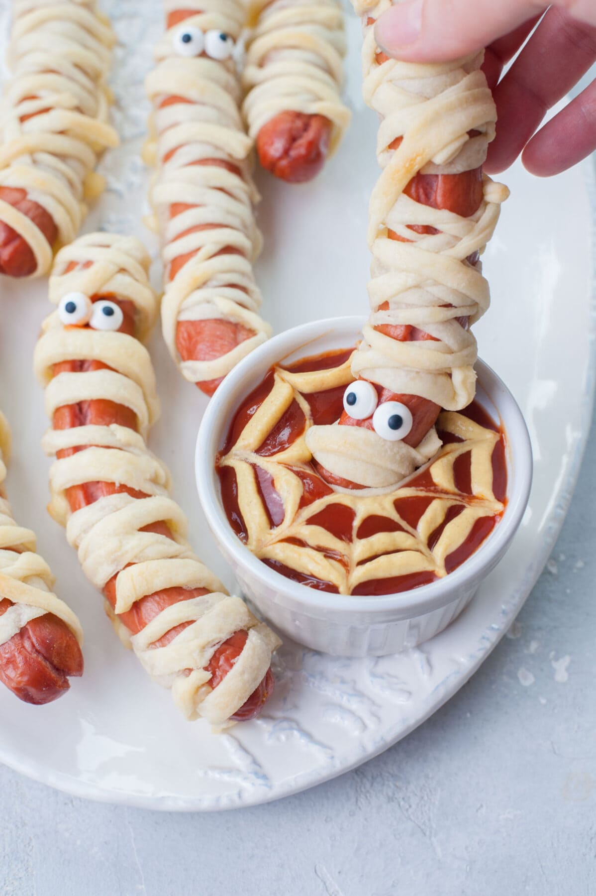 A mummy hot dog is being dipped in spider's web ketchup-mustard dip.