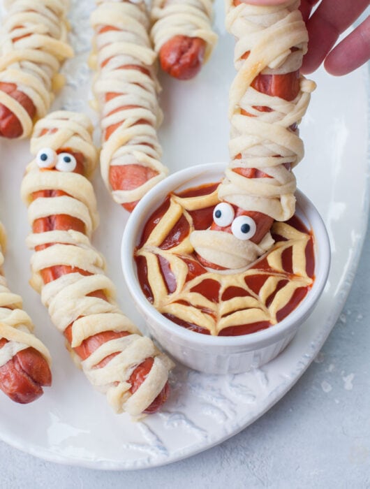Mummy hot dogs are being dipped in ketchup.