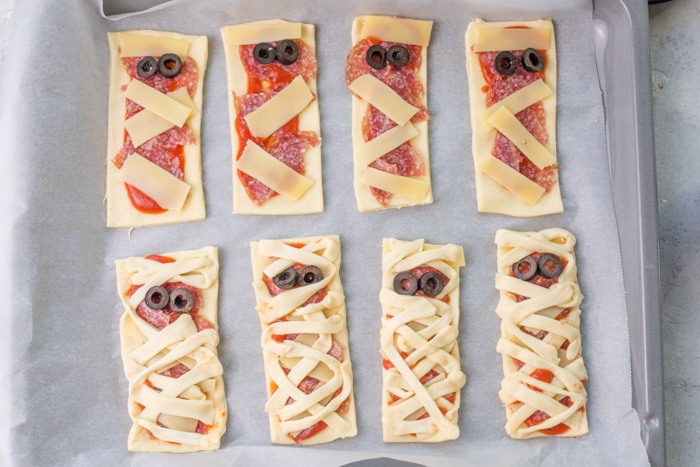 Pizza mummies on sheet pan lined with parchment paper ready to be baked.